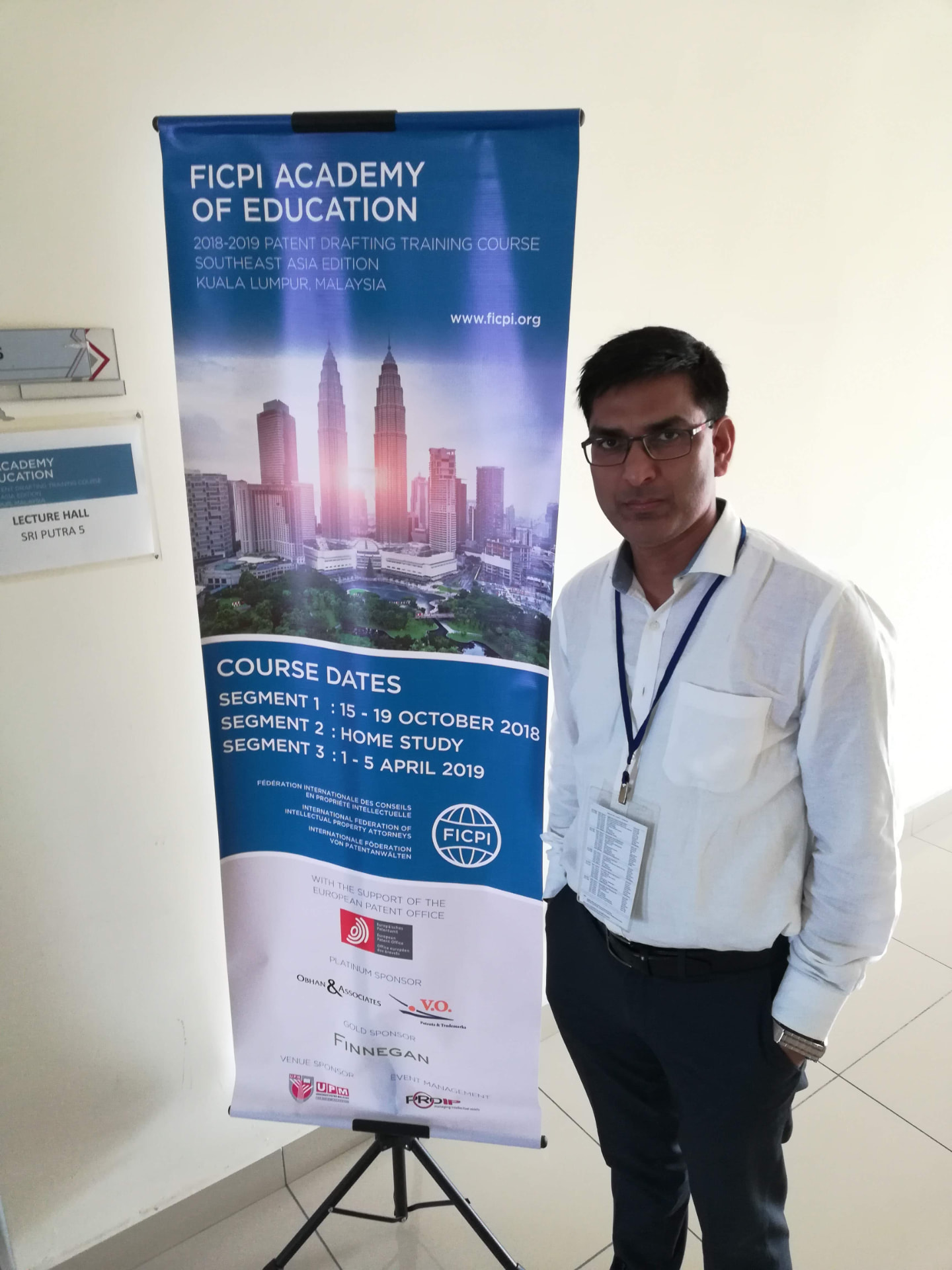 Founder of InKnowBiz Associates standing beside the FICPI Academy of Education SEAD patent drafting programme banner in Kuala Lumpur, Malaysia.