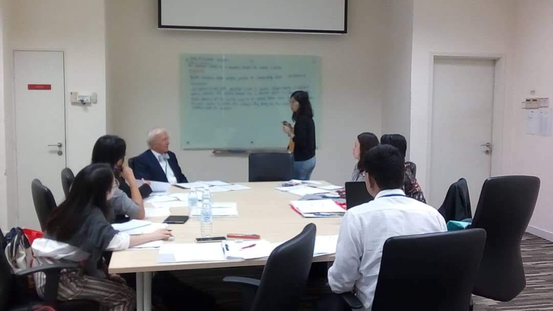 Course tutor leading a workshop discussion with participants beside a whiteboard.